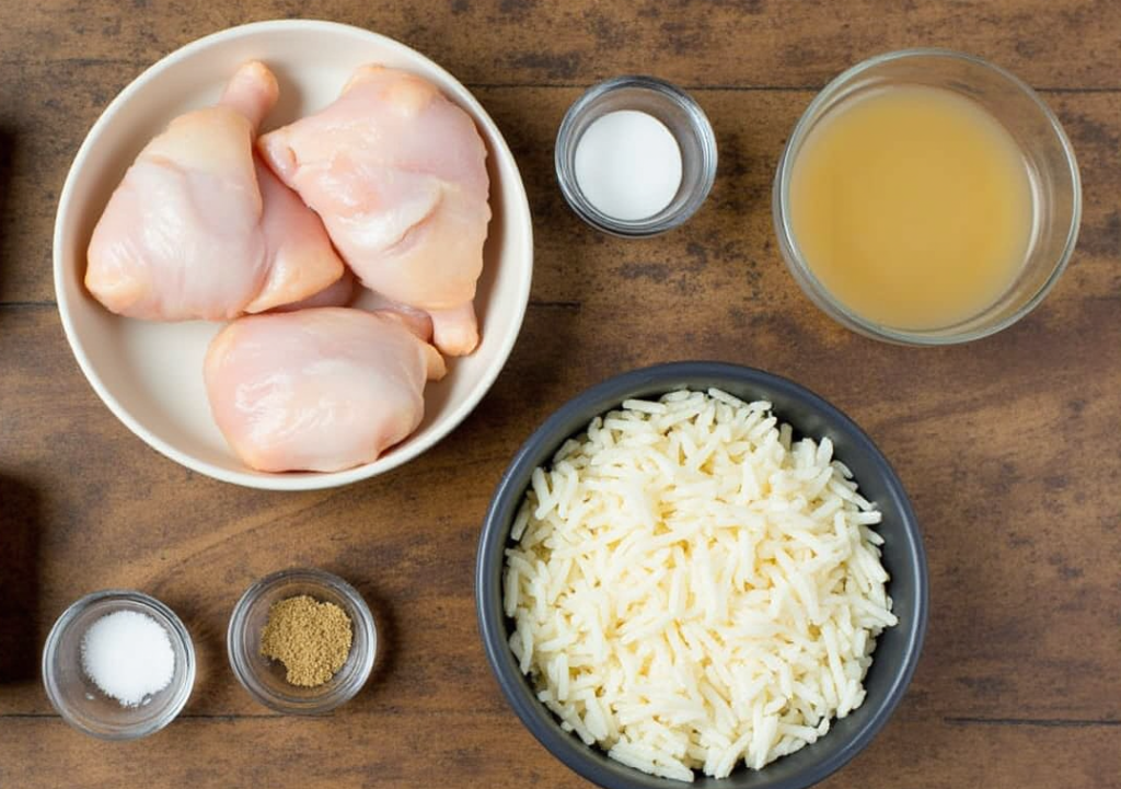 "Ingredients for the forgotten chicken recipe: raw chicken, uncooked rice, cream soup, chicken broth, and spices on a wooden table."